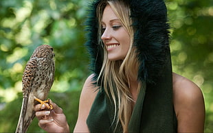 woman wearing green fur hood holding brown Shrike bird